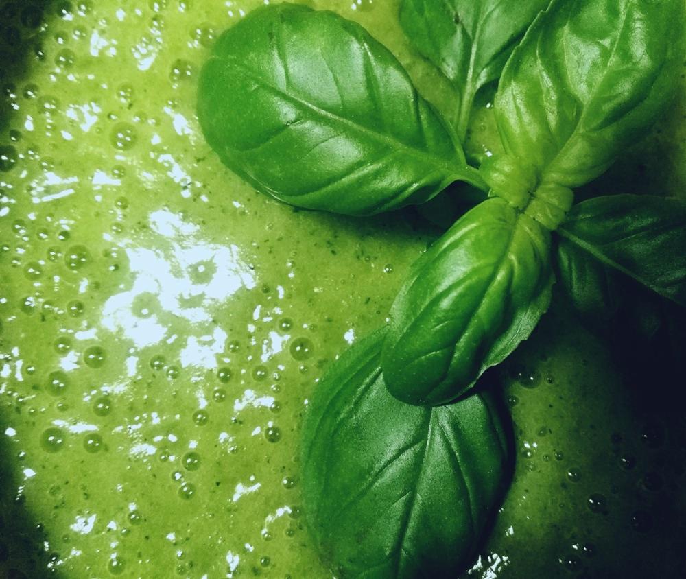 Jasnozielony koktajl z pęcherzykami powietrza, udekorowany świeżą bazylią o intensywnym zielonym kolorze.