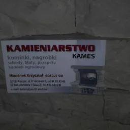 Zdjęcie wizytówki firmy kamieniarskiej 'KAMES' na tle ściany imitującej kamień, oferującej kominki, schody, blaty, parapety i inne wyroby z kamienia.