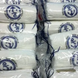 Stos białych ręczników frotte, każdy zapakowany w folię i ozdobiony niebieskim nadrukiem kotwicy z napisem 'Mikołaj 2017 WSD Świdnica'.