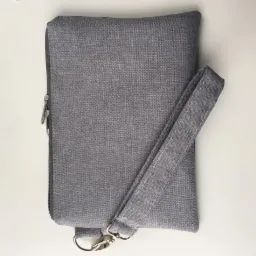 Szary, prostokątny pokrowiec z zamkiem błyskawicznym i uchwytem, leżący na białym tle, obok kilku różowych guzików.