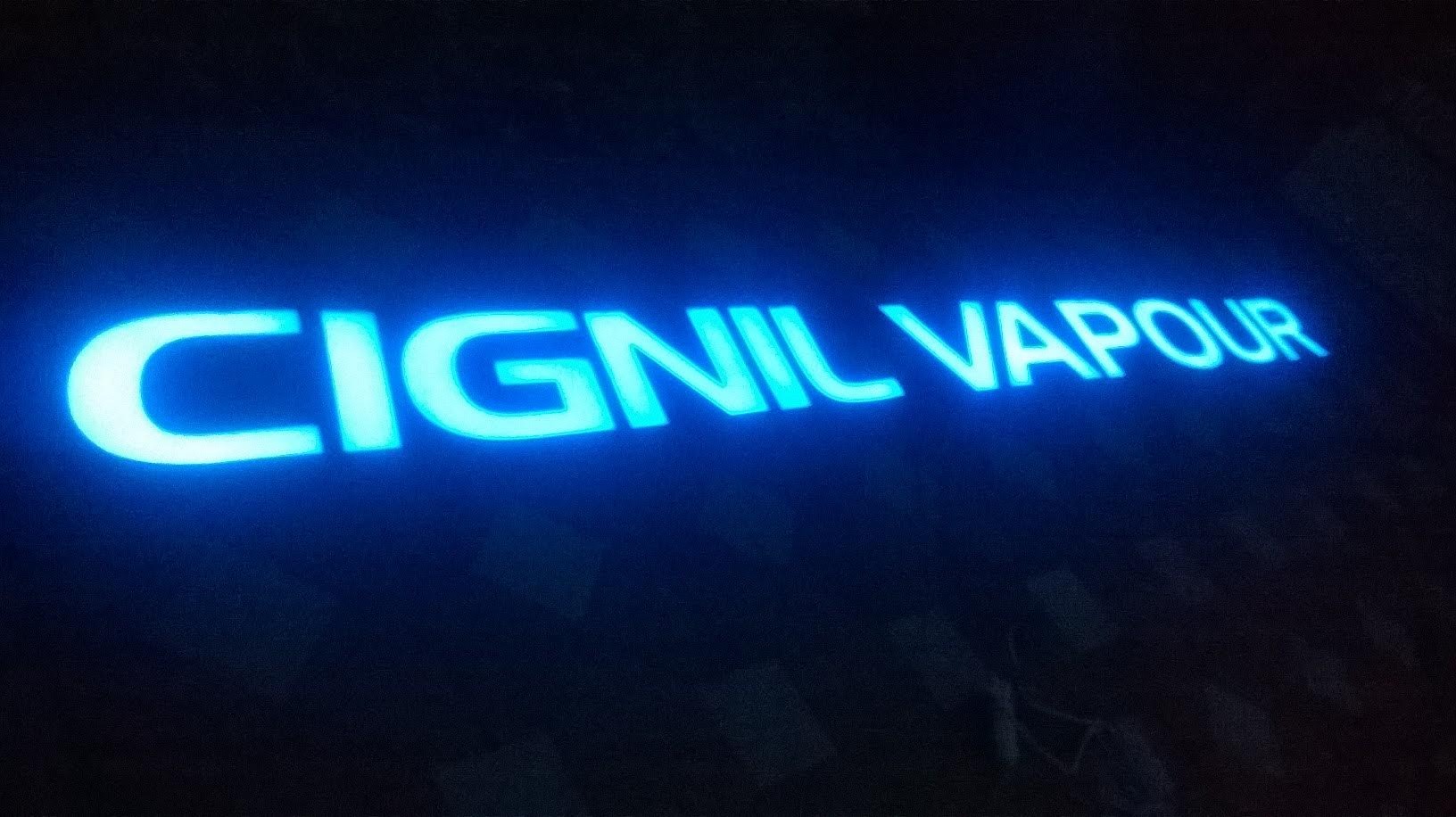 Podświetlane na niebiesko litery LED tworzące napis 'CIGNIL VAPOUR' na ciemnym tle.