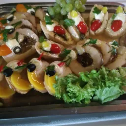 Dekoracyjna taca z przekąskami: roladki mięsne z sosem, grzanki z pomidorkami cherry i pesto, grzanki z brzoskwiniami i oliwkami, winogrona, sałata, całość na srebrnej tacy.