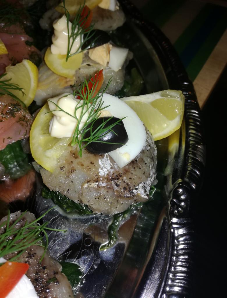 Filet śledziowy na srebrnej tacy, udekorowany cytryną, jajkiem, oliwką, kleksem majonezu i gałązką koperku, podany na szpinakowym podłożu.