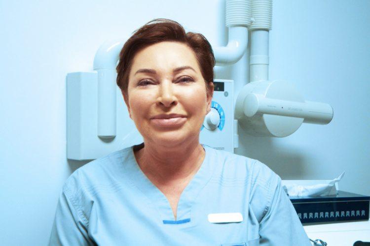 Portret uśmiechniętej kobiety w niebieskim uniformie na tle aparatu rentgenowskiego w gabinecie.