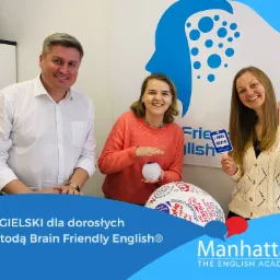 Trzech nauczycieli uśmiecha się do kamery, trzymając rekwizyty do nauki angielskiego, w tle logo szkoły językowej.