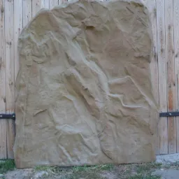 Dekoracyjna sztuczna skała LCM Wilbik ustawiona przed drewnianą bramą z metalowymi okuciami na tle ceglanego muru.