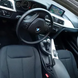 Wnętrze samochodu BMW z czarną tapicerką, widoczne fotele, kierownica, deska rozdzielcza i nawigacja.