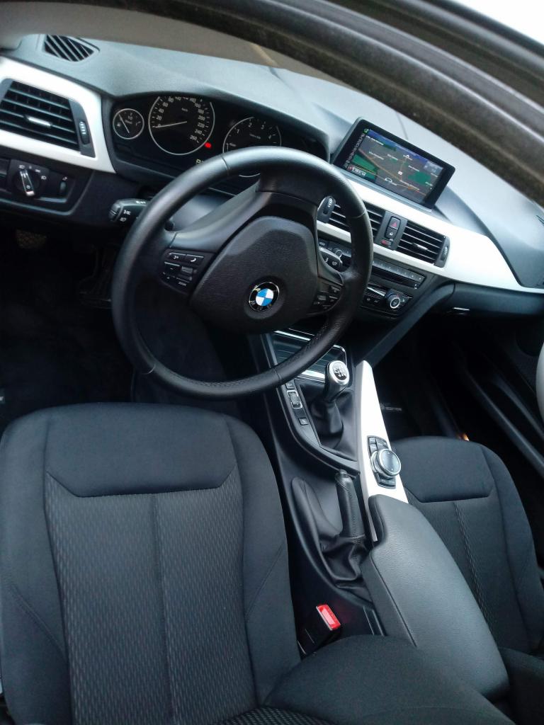 Wnętrze samochodu BMW z czarną tapicerką, widoczne fotele, kierownica, deska rozdzielcza i nawigacja.