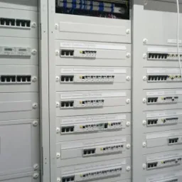 Rozdzielnica elektryczna z licznymi portami Ethernet i wyłącznikami, widoczne okablowanie w górnej części szafy.
