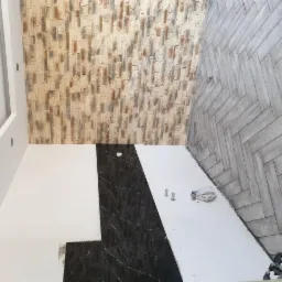 Wnętrze łazienki w trakcie remontu: ściana wykończona dekoracyjną cegłą, fragment ściany z czarnymi płytkami imitującymi marmur, podłoga z szarej mozaiki ułożonej w jodełkę, widoczne narzędzia...