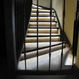 Schody drewniane z podświetleniem LED zamontowanym pod każdym stopniem, widoczne przez ozdobne metalowe barierki.