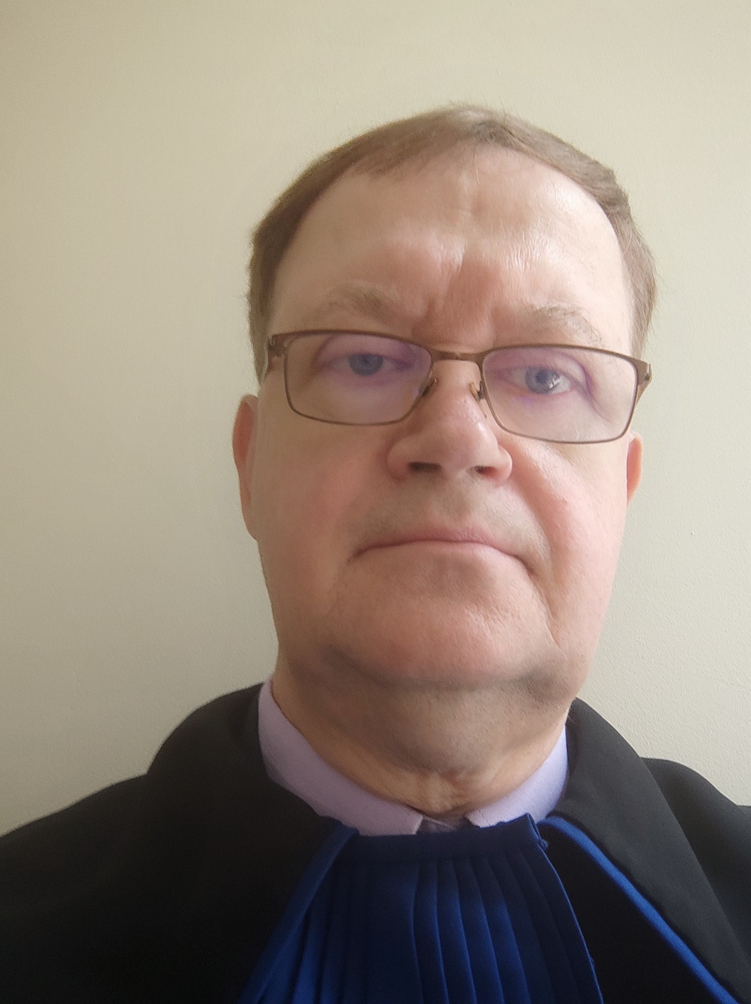 Portret mężczyzny w todze adwokackiej, z okularami, na jasnym tle. Widoczne detale stroju urzędowego i wyraz twarzy.