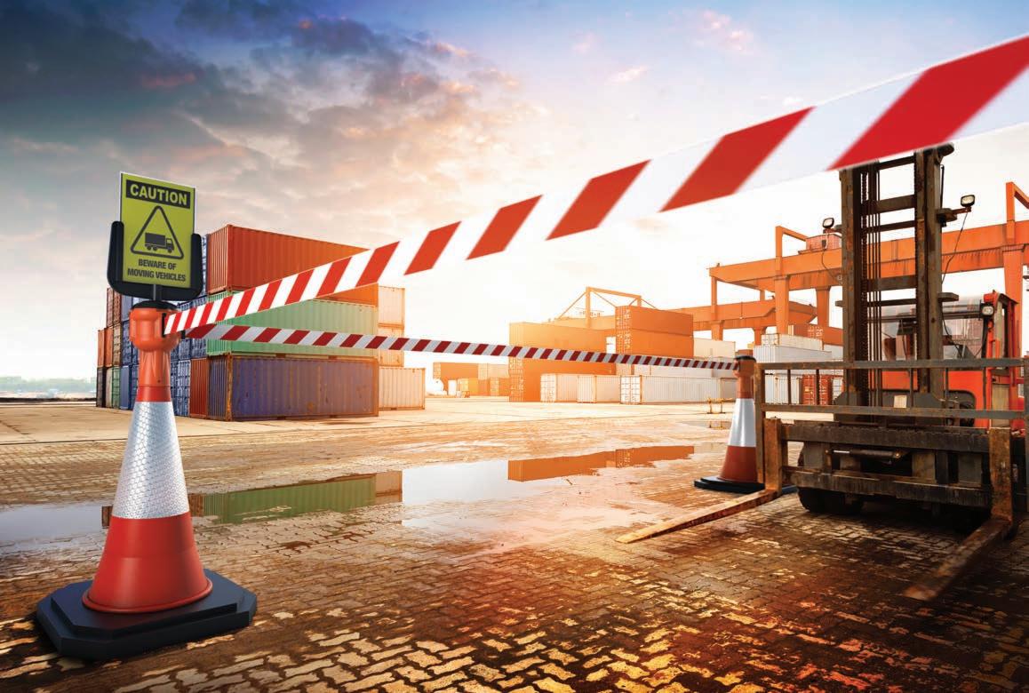 Strefa magazynowa z kontenerami i wózkiem widłowym, oznaczona taśmą ostrzegawczą i znakiem 'Uwaga! Ruch pojazdów', mokra nawierzchnia odbija promienie zachodzącego słońca.