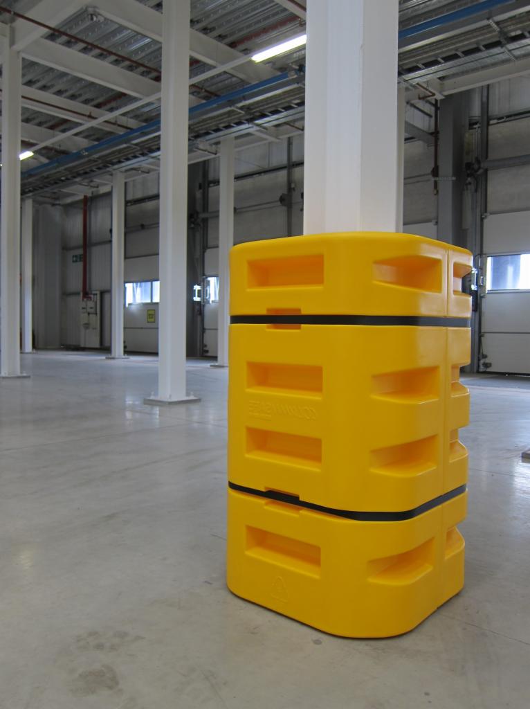 Żółta, modułowa osłona słupa w magazynie, z widocznymi otworami wentylacyjnymi i czarnymi pasami, na tle betonowej podłogi i białych słupów konstrukcyjnych.