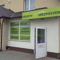 Fasada budynku z szyldem 'Kredyty Ubezpieczenia' i plakatem 'Auto Kredyt 24' z informacjami o kredytach, leasingu i rejestracji pojazdów.
