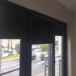 Ciemne, zwinięte osłony okienne w czarnej ramie, widok na ruchliwą ulicę z balkonu.