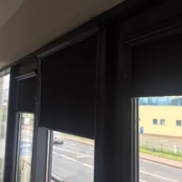 Częściowo zasłonięte, czarne okienne przesłony w nowoczesnym wnętrzu, widok na ulicę z przejeżdżającym samochodem.