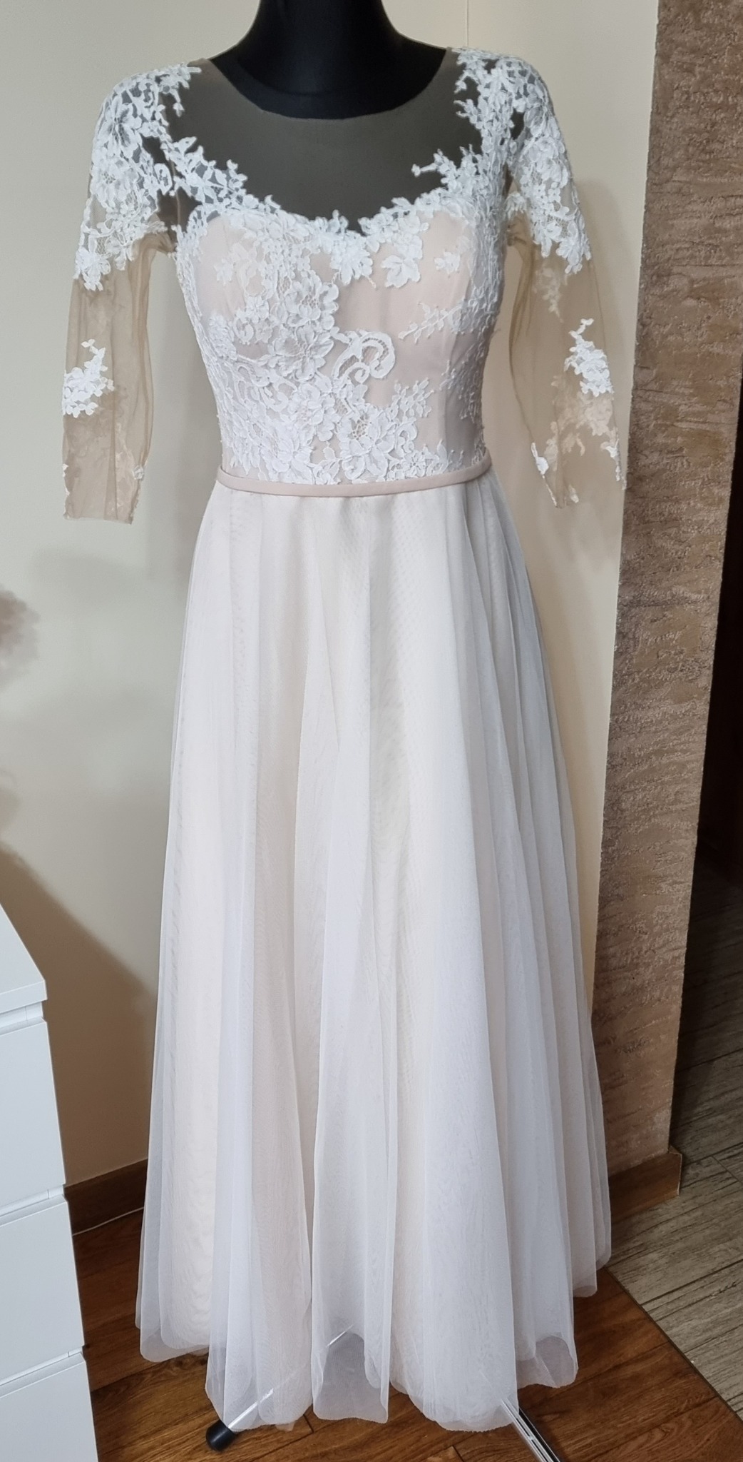 Suknia ślubna z koronkową górą i tiulowym dołem, prezentowana na manekinie w jasnym wnętrzu.