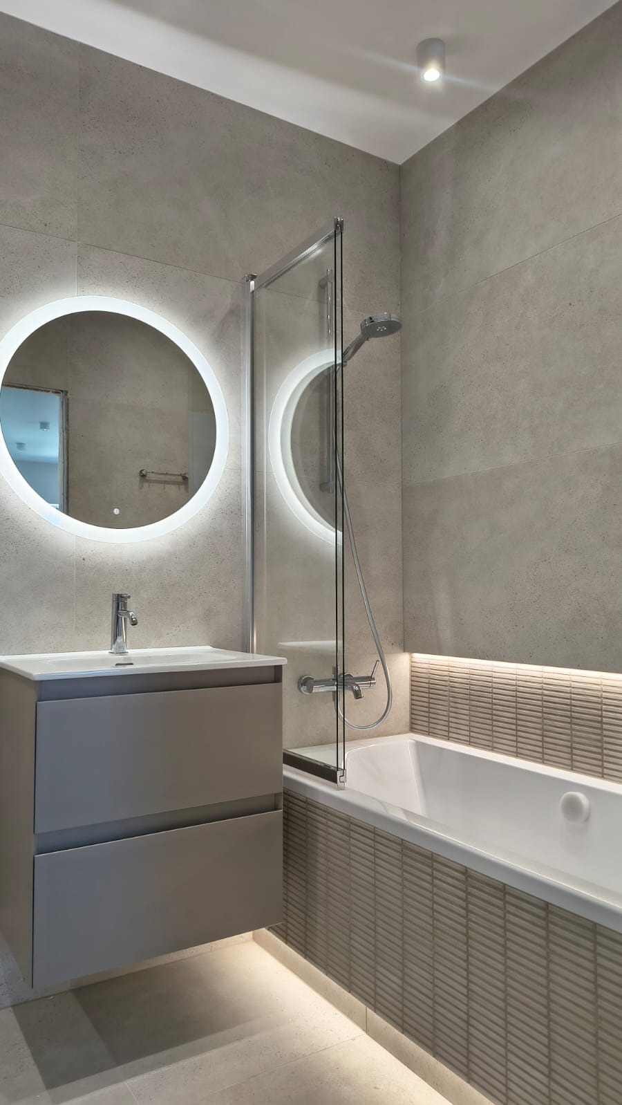 Nowoczesna łazienka w szarościach: podświetlane lustro, umywalka z szafką, przeszklony parawan nawannowy i mozaika. Minimalistyczny design.
