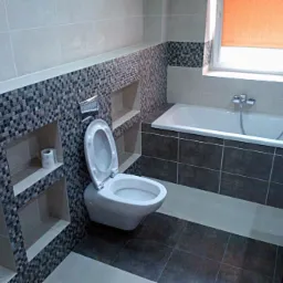 Wykończona łazienka z mozaiką na ścianie, wnękami z półkami, białą armaturą i brązowymi płytkami podłogowymi.