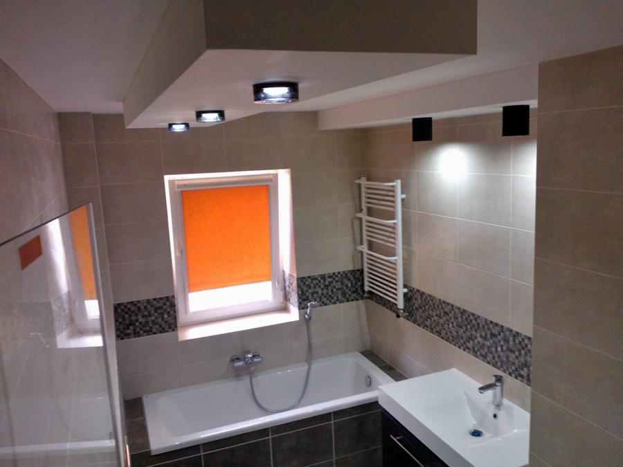 Jasna łazienka z beżowymi płytkami, ozdobnym pasem mozaiki, pomarańczową roletą w oknie i grzejnikiem drabinkowym