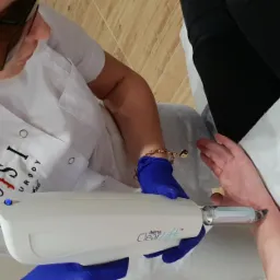 Zabieg laserowy ClearLift na skórze przedramienia wykonywany przez specjalistę w okularach ochronnych i niebieskich rękawicach, widoczne logo gabinetu na białym uniformie.