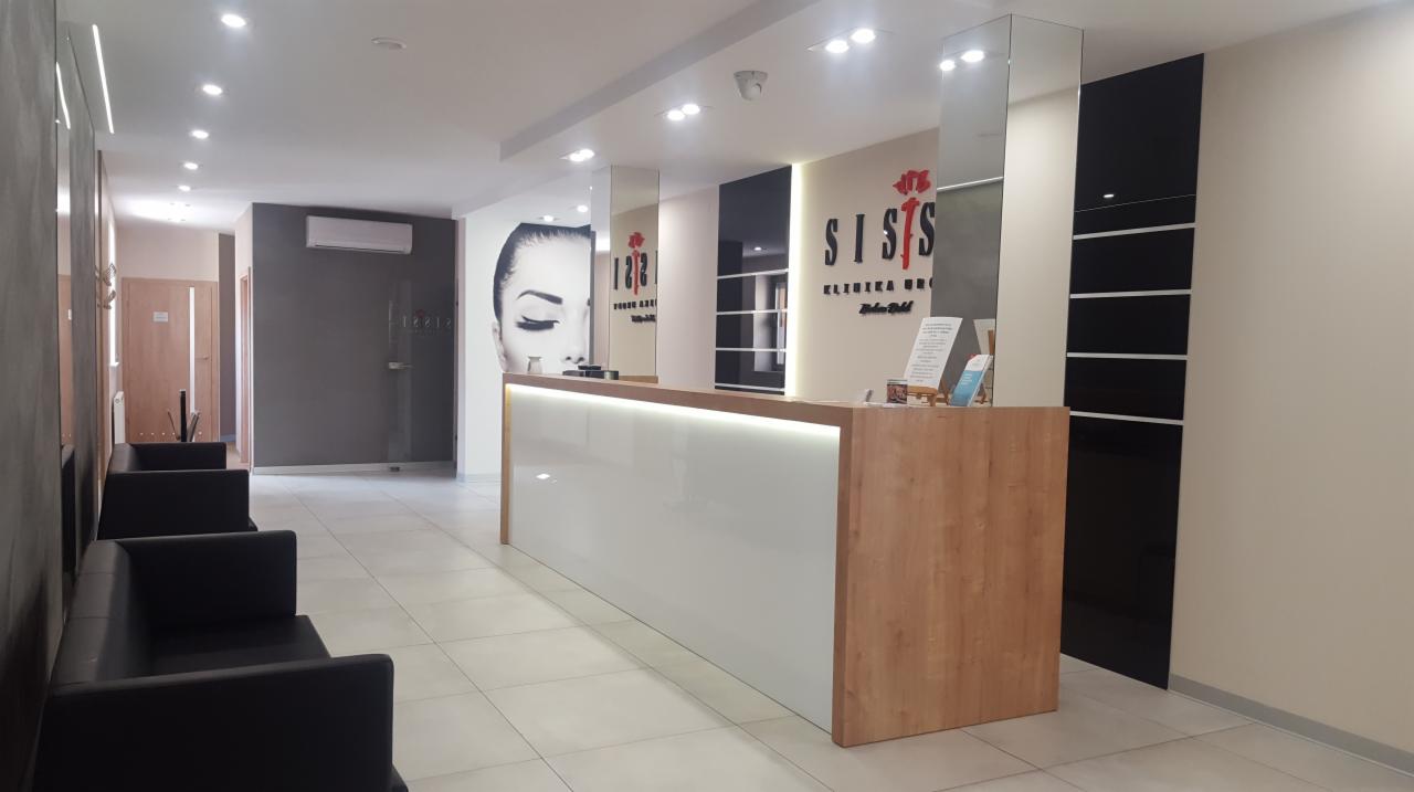 Wnętrze poczekalni kliniki z recepcją, czarnymi sofami i grafiką twarzy na ścianie.