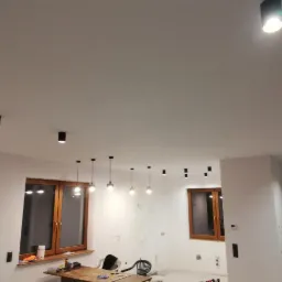 Nowoczesne oświetlenie sufitowe z czarnymi reflektorami punktowymi i wiszącymi lampami z żarówkami Edisona w surowym wnętrzu w trakcie wykończenia.