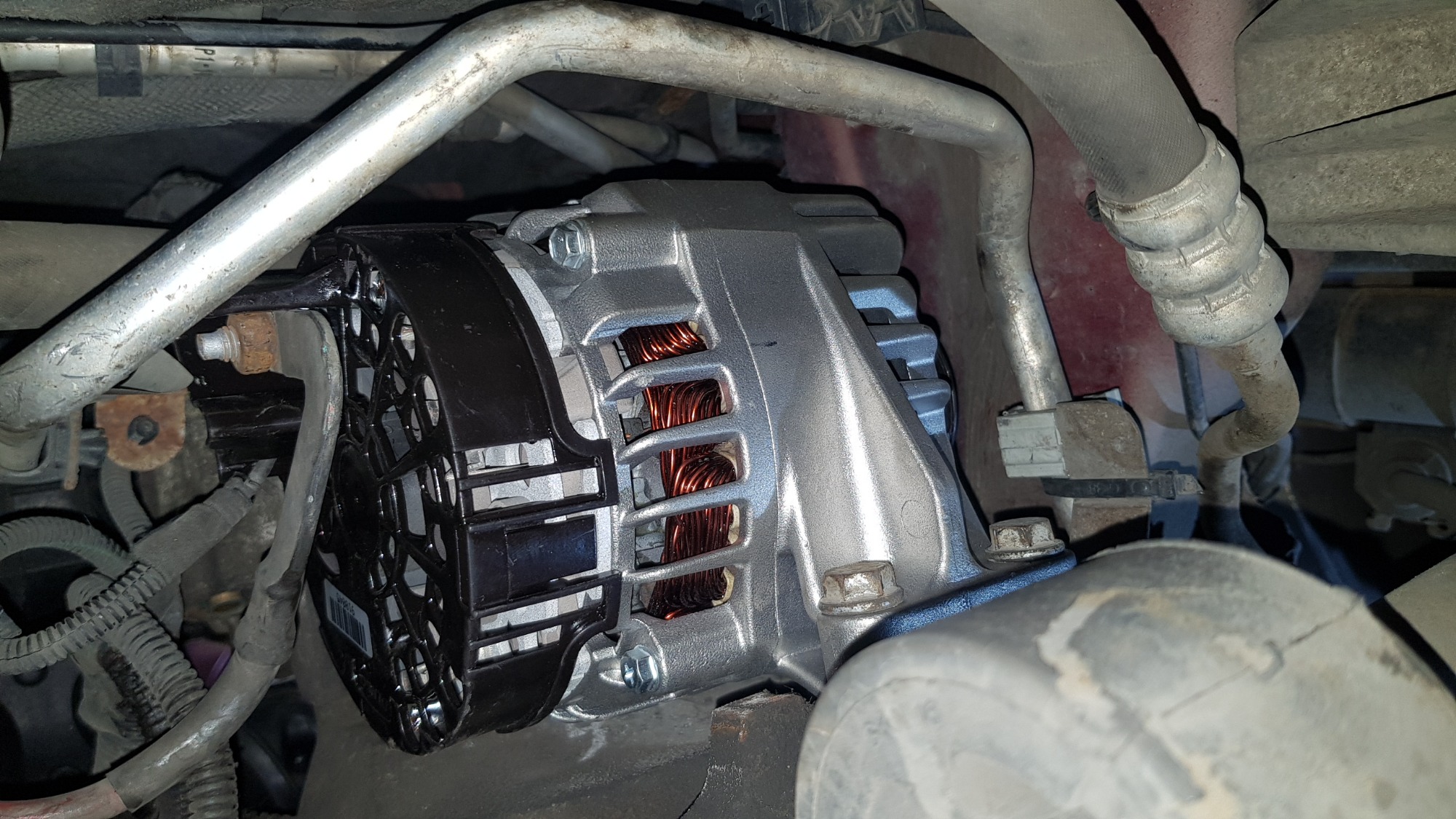 Nowy alternator zamontowany w komorze silnika samochodu, widoczne miedziane uzwojenia i czarna osłona wentylatora.