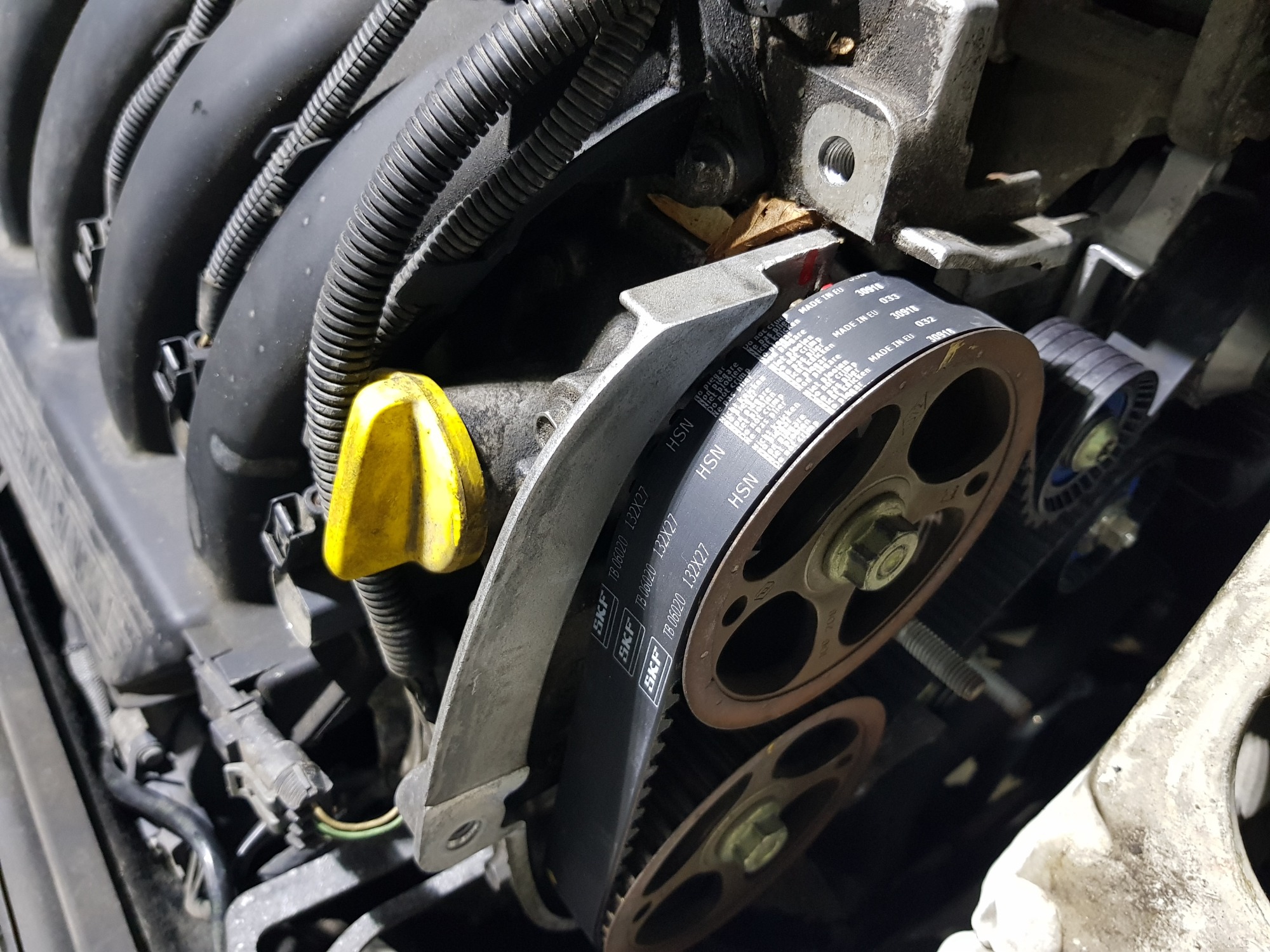 Szczegółowe ujęcie silnika samochodowego z widocznym paskiem rozrządu SKF, napinaczem i fragmentami osprzętu, ukazujące stan techniczny pojazdu.