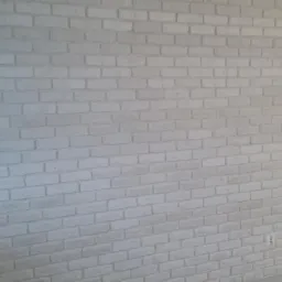 Ściana wykończona białymi cegłami dekoracyjnymi, widoczne gniazdko elektryczne i włącznik światła, fragment zielonej ściany w tle.