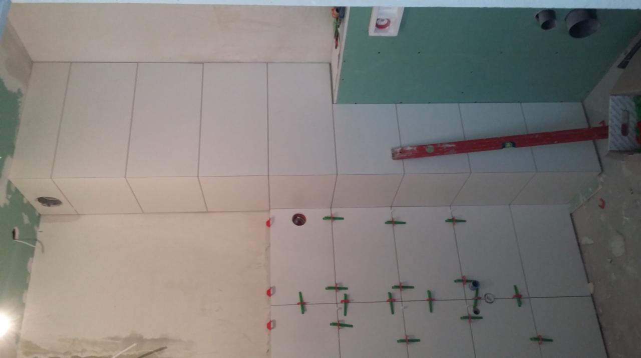 Układanie białych płytek w pomieszczeniu, widoczne krzyżyki dystansowe, poziomica i fragment ściany z płyt gipsowo-kartonowych.