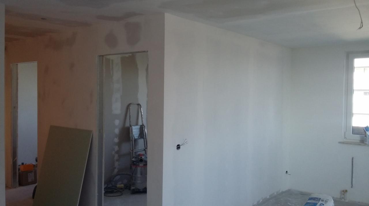 Pokój w trakcie odświeżania: świeżo wyszpachlowane ściany, widoczna drabina, płyta gipsowa oparta o ścianę oraz worek z gładzią na podłodze.