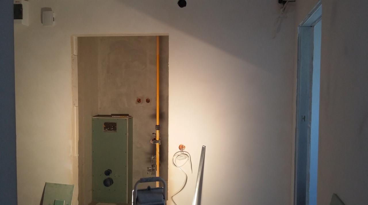 Wnętrze w trakcie prac wykończeniowych: ściany częściowo wyszpachlowane, widoczna instalacja gazowa, drabina i narzędzia, brak podłogi.
