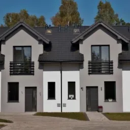 Nowoczesny bliźniak z szarymi oknami PCV, czarnymi drzwiami zewnętrznymi i balkonami z metalowymi balustradami, otoczony zielenią.