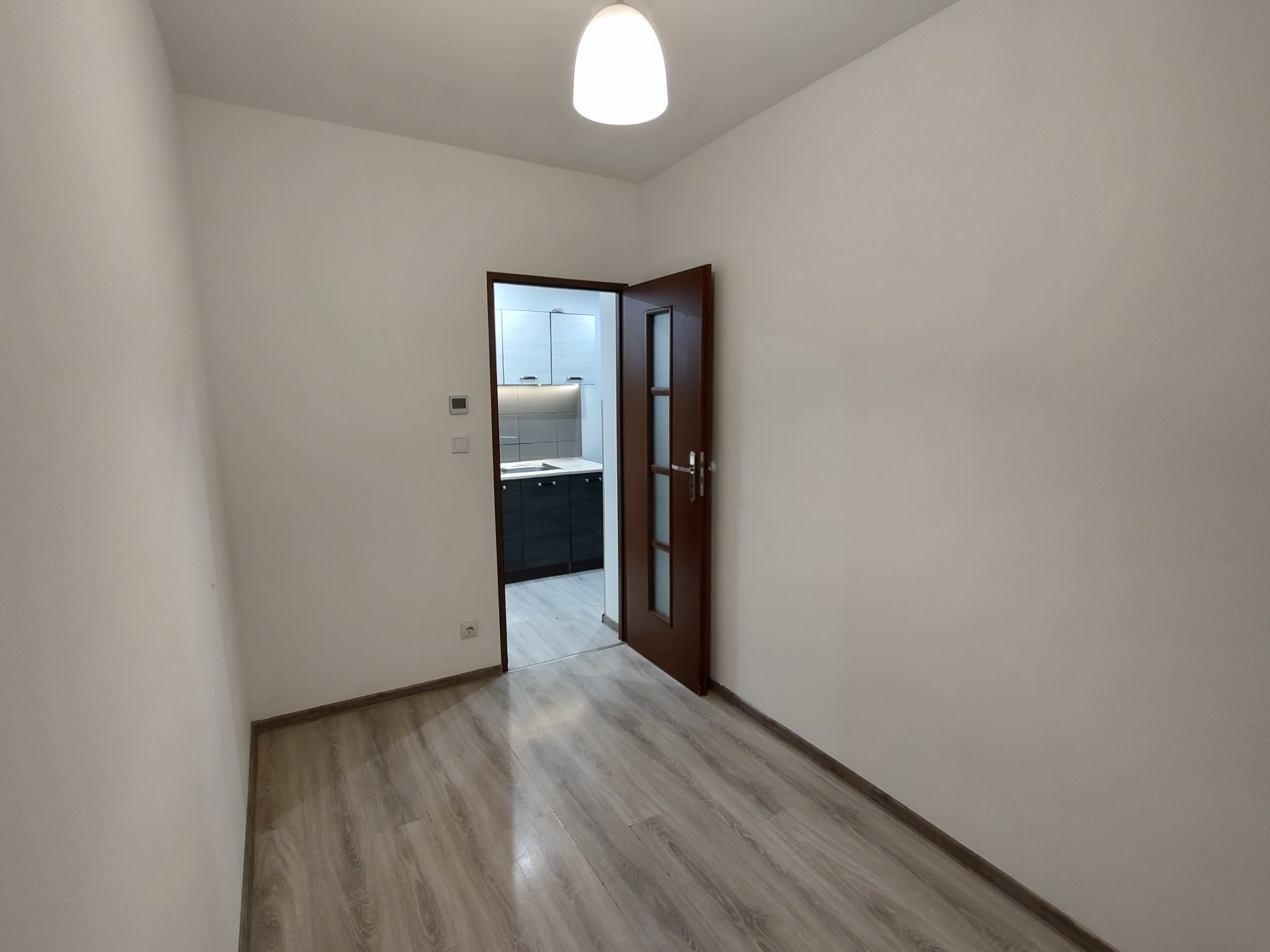 Jasne wnętrze po remoncie: świeżo pomalowane ściany, panele podłogowe w odcieniach szarości i otwarte drzwi do kuchni z nowoczesną zabudową.