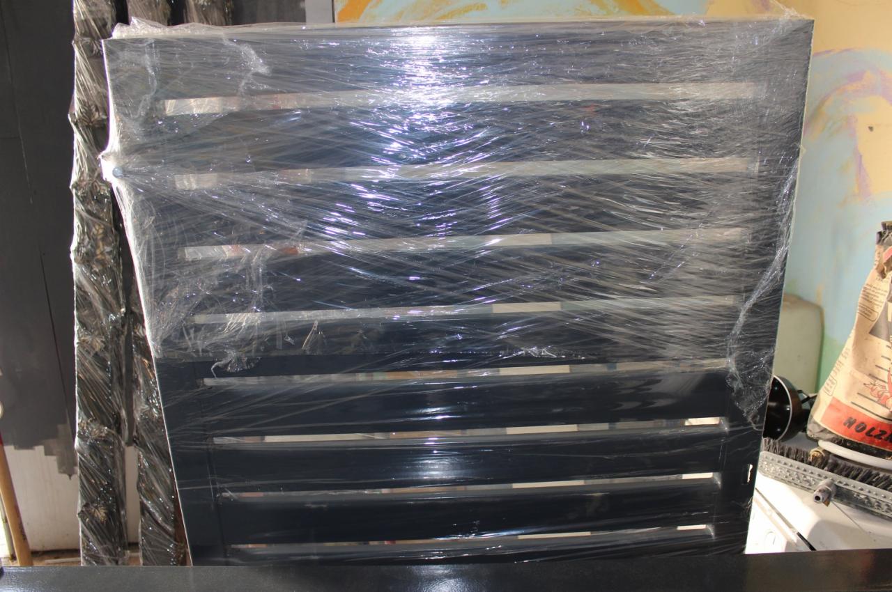 Ciemnoszara metalowa brama wjazdowa z poziomymi szczeblami, owinięta folią stretch na zapleczu warsztatu.