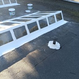 PHU FENIKS Robert Zmitrowicz - Płaski dach pokryty papą po uszczelnieniu świetlika dachowego i kominka wentylacyjnego białą masą uszczelniającą. Widoczne puszki z preparatem.