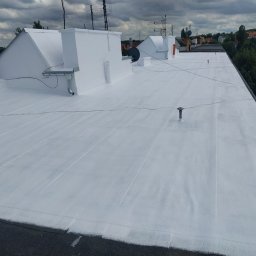 PHU FENIKS Robert Zmitrowicz - Biała, płaska powierzchnia dachu po renowacji, widok z góry. Widoczne kominy, anteny i elementy wentylacyjne. W tle zabudowa miejska i zieleń.