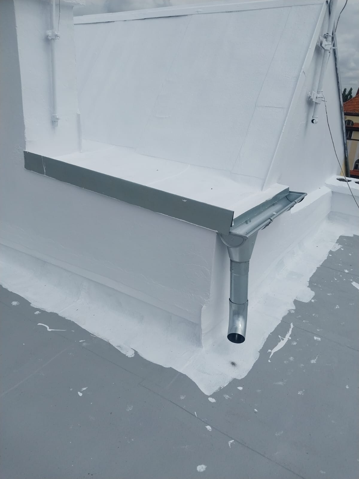 Biały, płaski dach po renowacji w Gdańsku, z widoczną metalową rynną i obróbkami blacharskimi. Świeżo nałożona warstwa hydroizolacji. Detal dachu po remoncie.