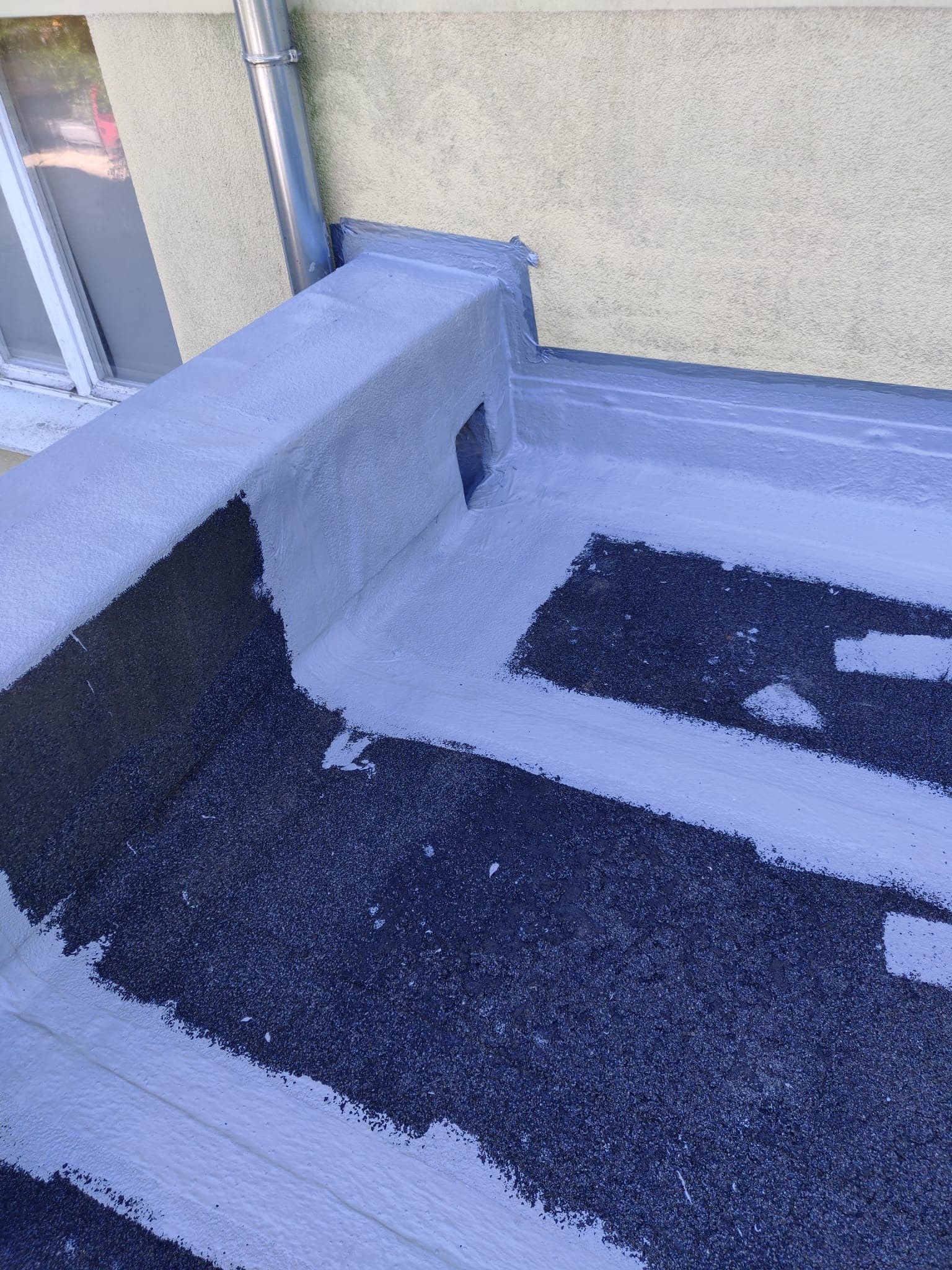 Szczegółowe ujęcie płaskiego dachu po hydroizolacji, z widoczną warstwą izolacyjną w kolorze szarym i fragmentem rynny spustowej. Widoczna faktura pokrycia dachowego.