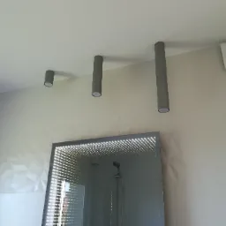 Nowoczesna łazienka w Tarnowskich Górach z podświetlanym lustrem infinity, trzema cylindrycznymi lampami sufitowymi w odcieniach szarości i dekoracyjną ścianą z trójwymiarowych paneli.