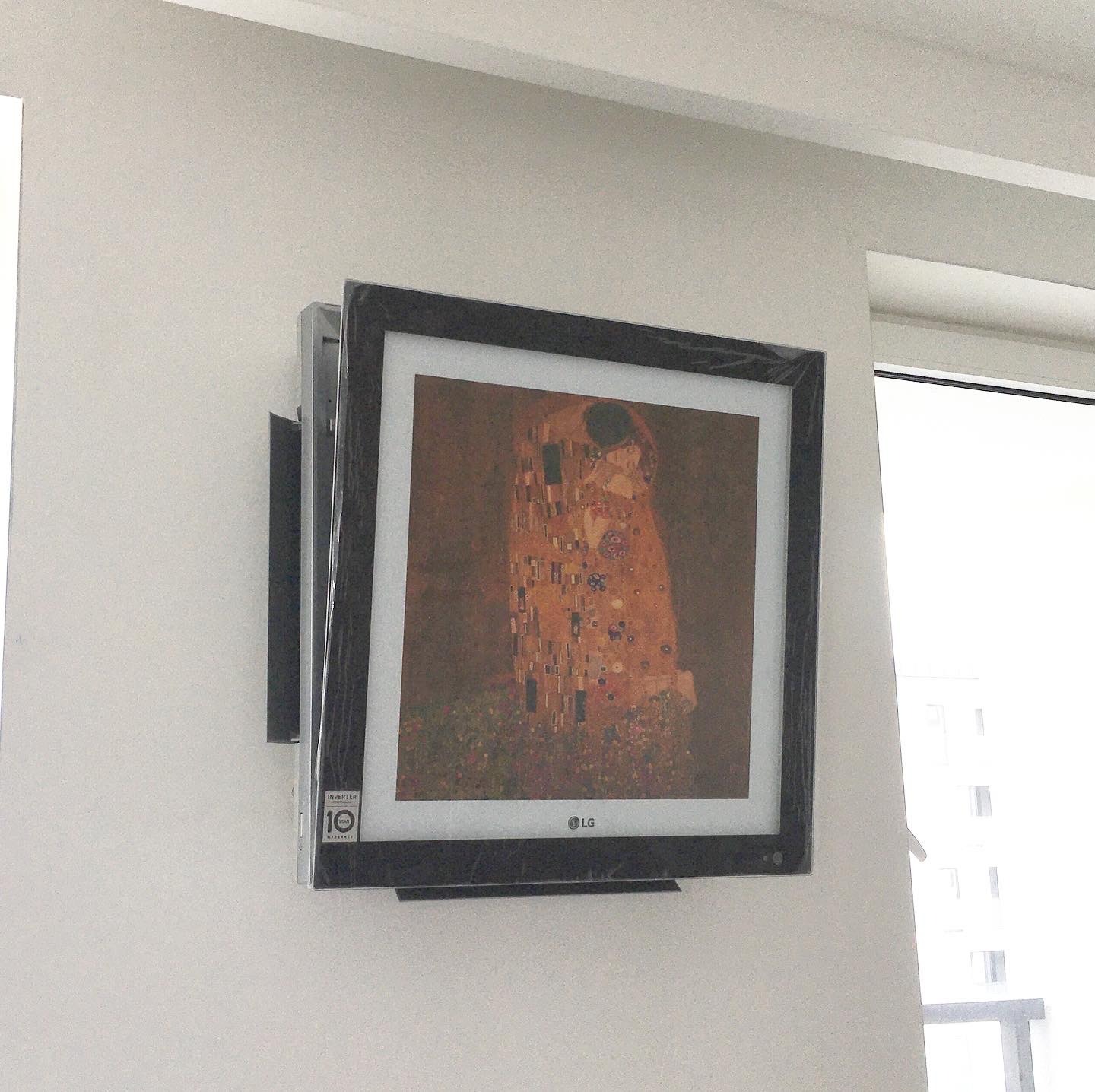 Telewizor LG w ramie, wyświetlający obraz 'Pocałunek' Gustava Klimta, zawieszony na białej ścianie. Widoczna naklejka '10 lat gwarancji' w lewym dolnym rogu.