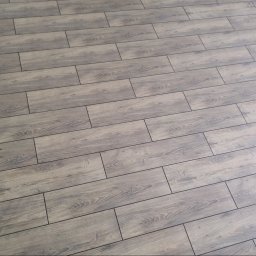 Usługi glazurnicze Dawid Świdurski - Ukończona podłoga z paneli imitujących drewno, ułożona pod kątem. Widoczne delikatne wzory słojów i fugi. Oświetlenie z prawej strony dodaje jasności.