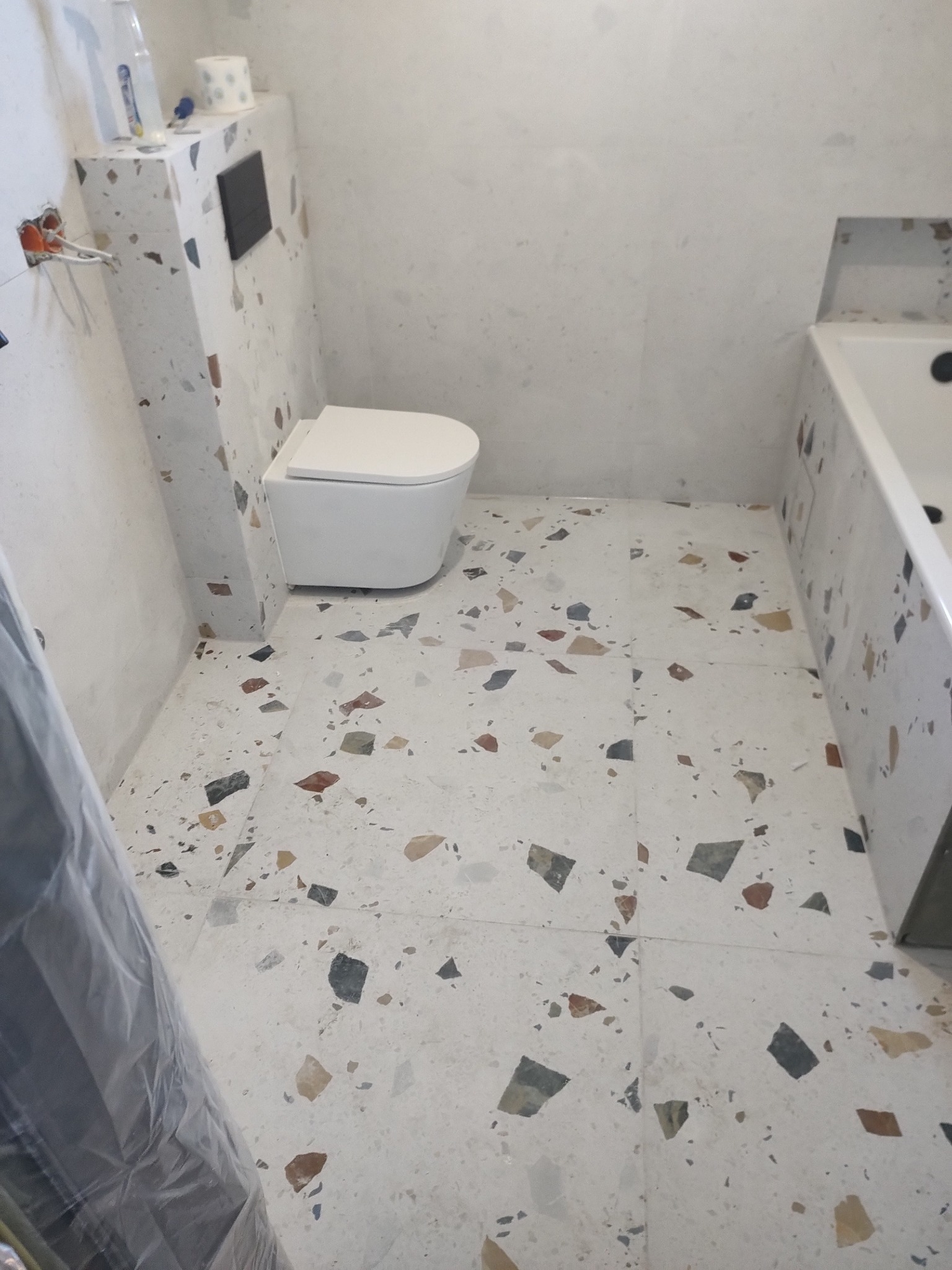 Wykończona łazienka w Śremie z toaletą i wanną, płytki podłogowe i ścienne w stylu lastryko, widoczne instalacje elektryczne.