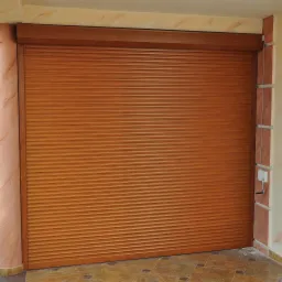 Zamknięta, brązowa osłona okienna zewnętrzna z widocznym mechanizmem sterowania na ścianie budynku.