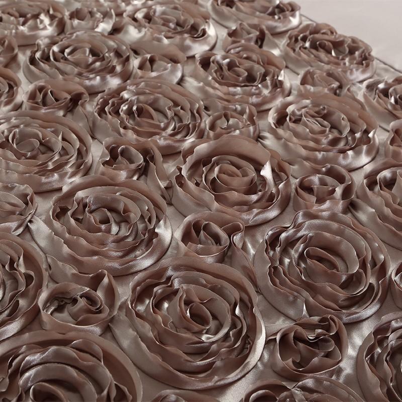 Satynowa tkanina w kolorze taupe z aplikacjami w kształcie róży, widoczne delikatne cieniowanie i faktura materiału.