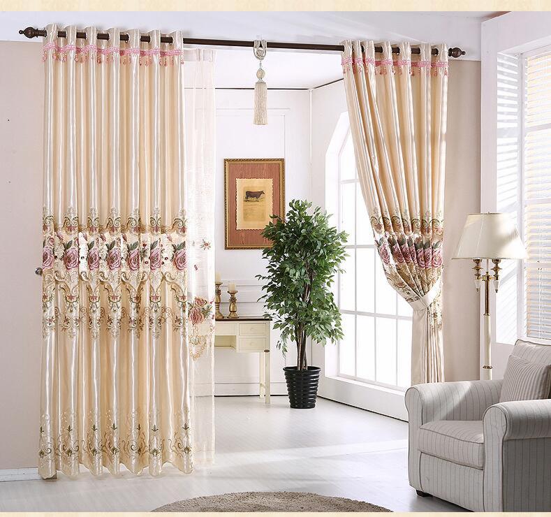 Eleganckie, kremowe zasłony z kwiatowym haftem w salonie, częściowo przesłonięte przezroczystą firanką, z widocznym fragmentem białego fotela i rośliną doniczkową.