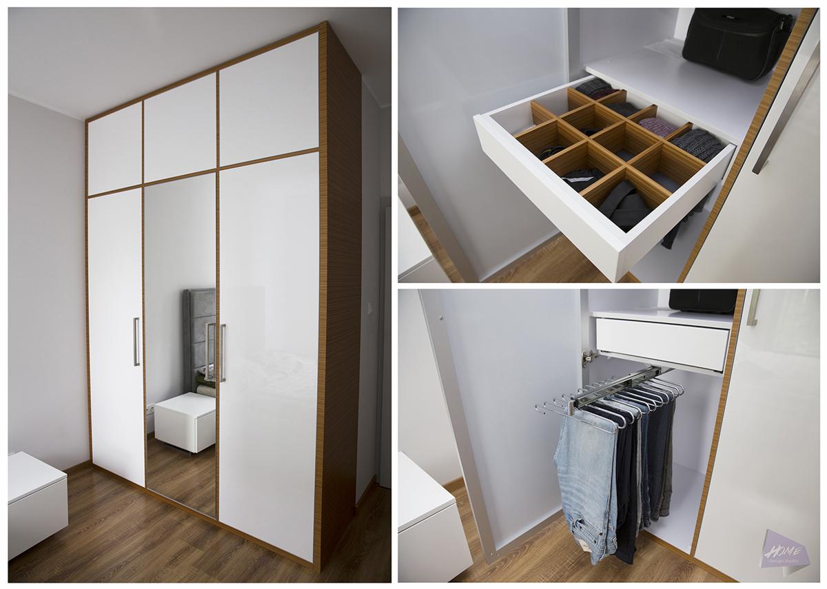 Nowoczesna szafa z białymi frontami i drewnianymi akcentami, z widocznym systemem organizacji wnętrza: wysuwana szuflada z przegródkami na akcesoria i wieszak na spodnie.