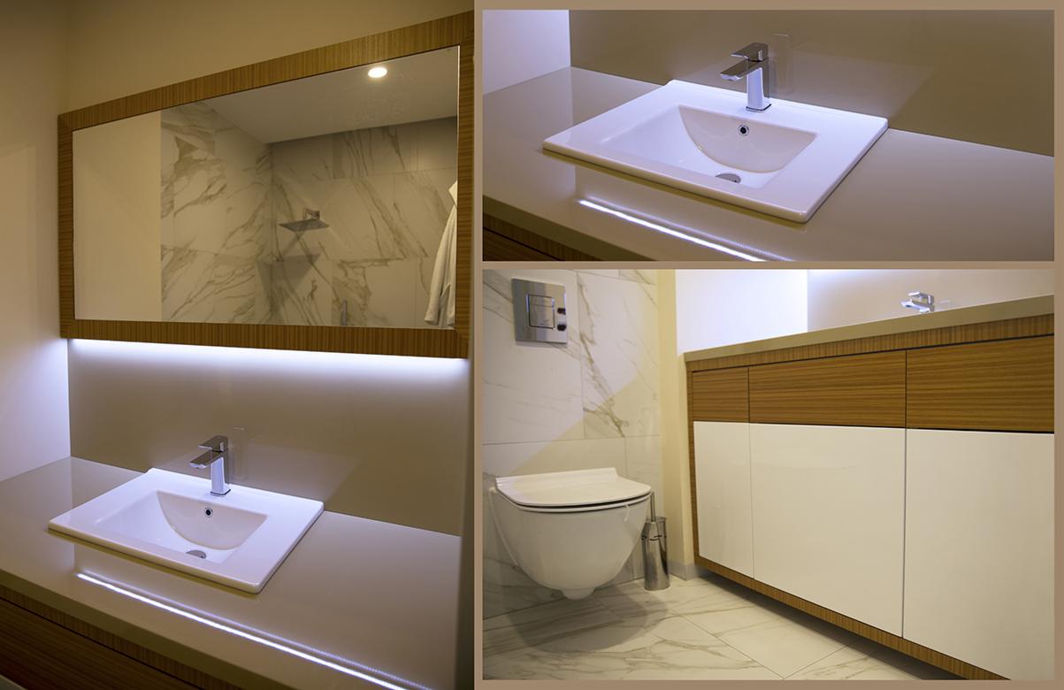 Nowoczesna łazienka z białymi płytkami imitującymi marmur, umywalką nablatową z chromowaną baterią, podświetlanym lustrem w drewnianej ramie oraz szafką pod umywalką z frontami w kolorze drewna...